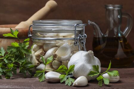 still life in horizontal view of an oil pourer, mortar, airtight glass jar with garlic cloves, parsley and garlic headの写真素材