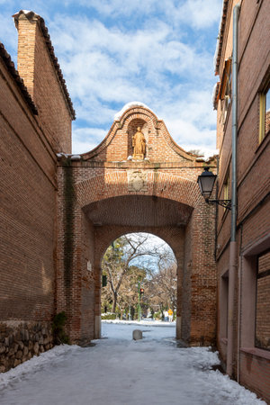 vertical view of arch of saint bernard in the city of alcala de henares with O'Donnel park in the background on a sunny day after a snowfallの写真素材