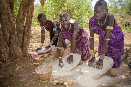 JINKA, ETHIOPIA - 10 August: unidentified beautiful girls from Mursi tribe in Mago National Park, Jinka, on 10 august 2014. Women are grinding cereals with a stone to prepare flourのeditorial素材