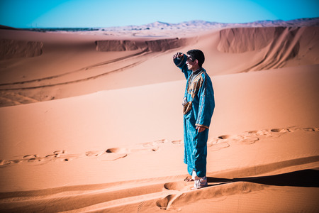 Merzouga Morocco  27 March 2015: unidentified tuareg looking for something in the dunes of Sahara desert. Tuareg are called blue men for their traditional dressesのeditorial素材