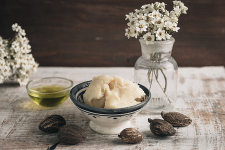 Two bowl of shea butter and oil with shea nuts on shabby wooden table.の写真素材