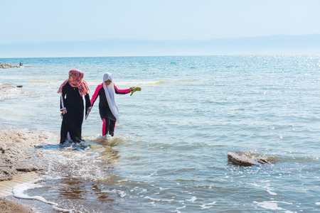 DEAD SEA, JORDAN - AUGUST 12, 2016: two unidentified women walk on the salted coast of the Dead Sea, in Amman Beach. One of them dress the burkini.のeditorial素材