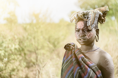 MAGO NATIONAL PARK, ETHIOPIA - AUGUST 19, 2015:  unidentified Mursi woman stands in the grass with beautiful decorations on her face. Body painting is very important in Mursi tribeのeditorial素材