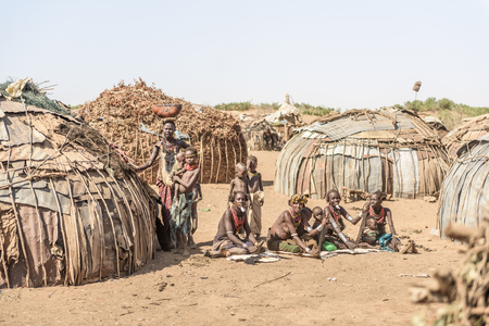 OMORATE, ETHIOPIA - AUGUST 17, 2015: unidentified Dassanech women work sitting in the ground in their village. Their huts have the shape of a dome made of branches and metal sheetsのeditorial素材