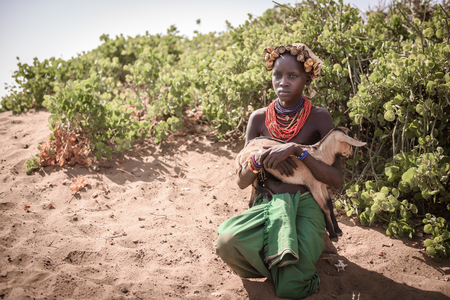 OMORATE, ETHIOPIA - AUGUST 17, 2015: unidentified girl from Dassanech tribe hold a little goat. She...