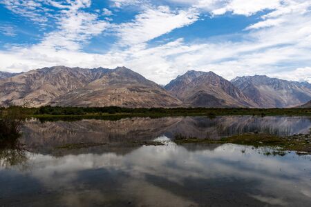 High mountains in the Nubra Valley, India, reflected in a riverの写真素材