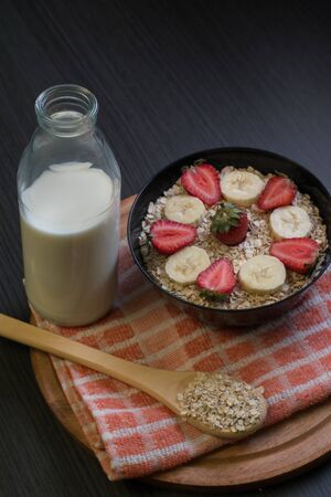 Medium shot of a bowl with oatmeal and slices of banana and strawberry with a bottle with milk and a wooden spoon with oatmealの写真素材