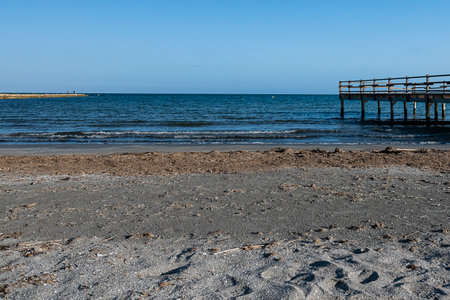 Serene beach with soft sand and gentle waves lapping at the shore, featuring a sturdy wooden pier.の写真素材