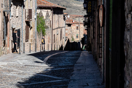 Visitors stroll along a charming cobblestone street in a rustic village under bright sunlight, enjoying the scenery.の写真素材