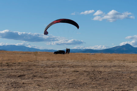 Two individuals prepare for paragliding in a spacious field with distant mountains under a bright sky.の写真素材