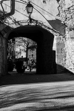 A person strolls out of a stone archway, surrounded by potted plants in a historical town setting.の写真素材