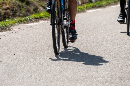 Two cyclists pedal on a winding rural road, enjoying the sunny weather and beautiful surroundings.の写真素材