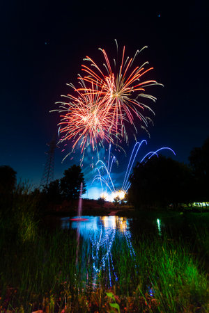 Bright fireworks explode in vibrant colors over a tranquil lake, reflecting the dazzling display as night falls.の写真素材
