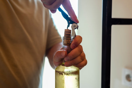 Person uncorking wine bottle in cozy indoor setting during afternoon gatheringの写真素材