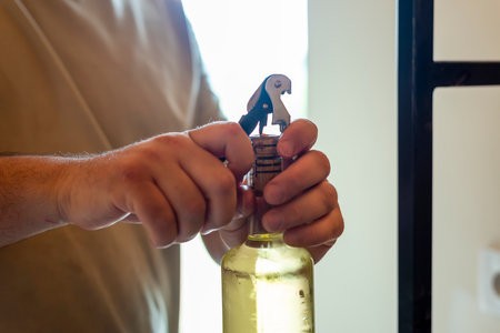 Hands skillfully removing a cork from a wine bottle in a warm and inviting kitchen atmosphere.の写真素材