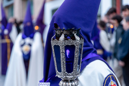 Participants in a colorful parade wear robes and hoods, holding candles during an evening...