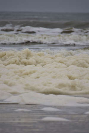 Waves and sea foam on a beach of the North Sea on a cloudy day