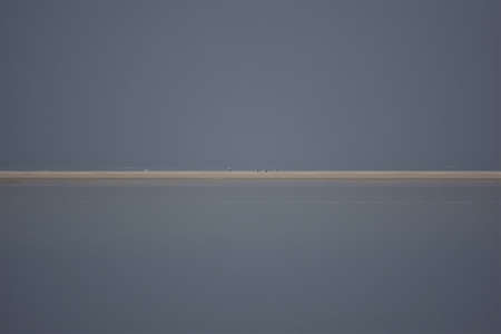 Sandbank at high tide surrounded by water against a clear blue skyの写真素材