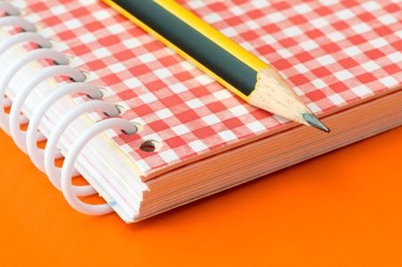 pencil and notebook over an orange background