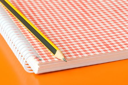 pencil and notebook over an orange backgroundの写真素材