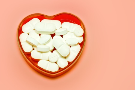 plastic heart holding some pills over pink