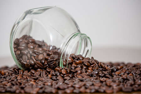Glass with red lid pouring over the table in beans coffee powder straight from the farm.の写真素材