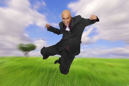 Powerful and  happy businessman jumping in a green fieldの写真素材