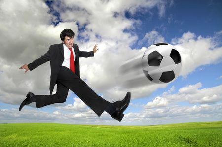 Businessman in a acrobatic pose kicking a soccer ball in a green fieldの写真素材