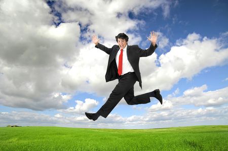 Young happy businessman jumping in a green fieldの写真素材