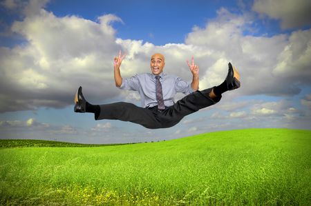 Happy businessman jumping high  in a green fieldの写真素材