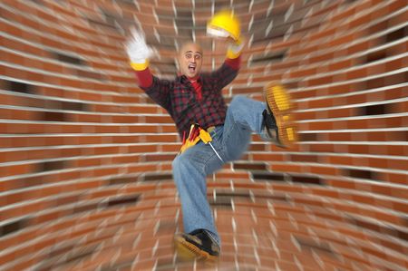 Construction worker falling with a brick wall as backgroundの写真素材