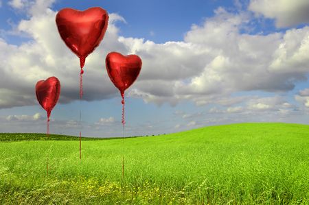 Red balloons in  a grass field with blue cloudy skyの写真素材