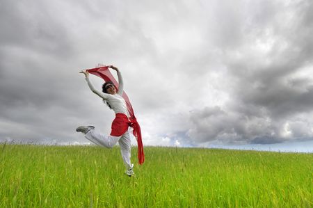 Woman jumping high in a green field with a scarfの写真素材