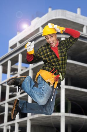 Happy construction worker jumping with a building as backgroundの写真素材