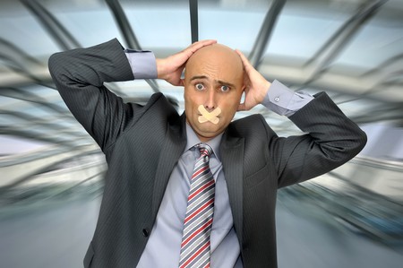 Distressed businessman with hands in his head and mouth covered with band aidの写真素材