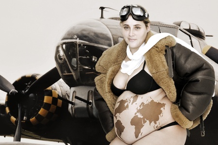Pregnant woman with pilot jacket and world map in her belly and a bomber as backgroundの写真素材