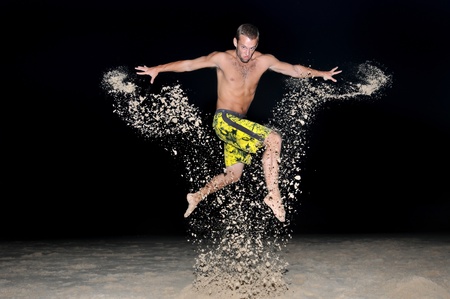 Muscular young man jumping with sand in the beach by night