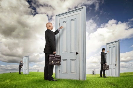 Businessmen or salesmen with briefcases knocking at several doors in a green fieldの写真素材