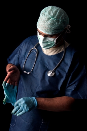 Doctor taking of his gloves in a dark backgroundの写真素材