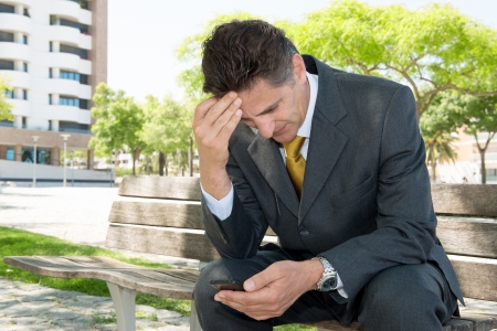 Worried businessman in a park bench with cellphoneの写真素材