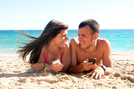 Teenagers on the beach with cellphones checking messagesの写真素材