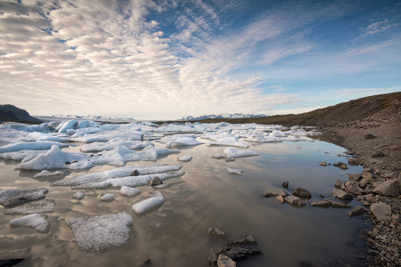 Reflections in Fjallsarlon lagoon in Iceland, by sunset