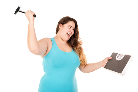 Desperate large girl punishing a weight scale with a hammer isolated in whiteの写真素材