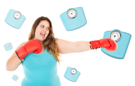 Large girl with boxing gloves hiting a weight scale isolated in whiteの写真素材