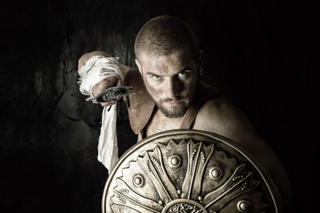 Gladiator posing with shield and sword in a dark backgroundの写真素材
