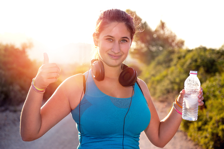 Beautiful girl jogger outdoors drinking water at sunsetの写真素材