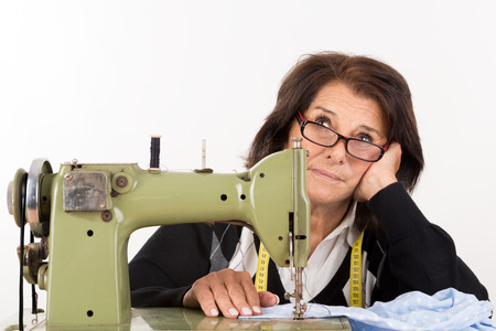 Stressed senior woman with sewing machine isolated in white