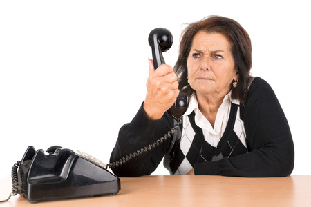 Angry senior woman with old telephone isolated in whiteの写真素材