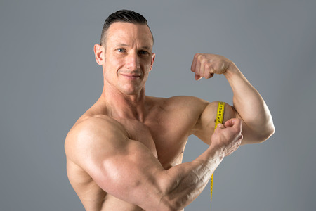 man with powerful biceps using a measuring tapeの写真素材