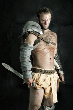 Ancient warrior or Gladiator posing against a dark background with swordの写真素材